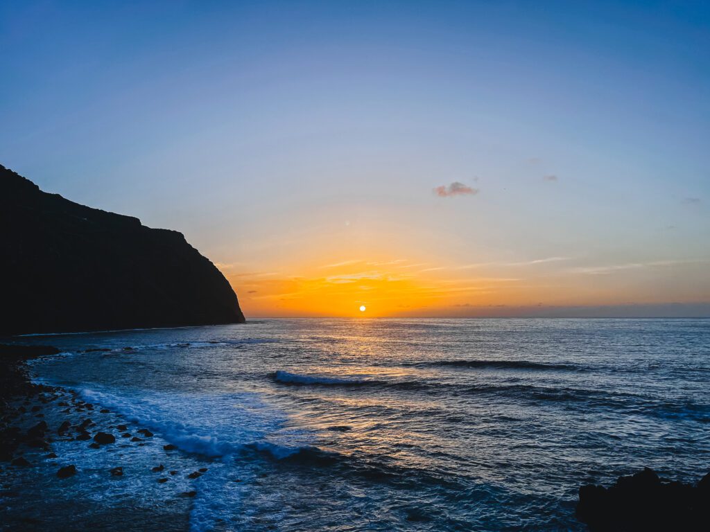 Panoramisch uitzicht over de ondergaande zon in Porto Moniz. Je ziet de zon zakken in de zee en dit geeft een oranje en gele gloed aan de lucht.