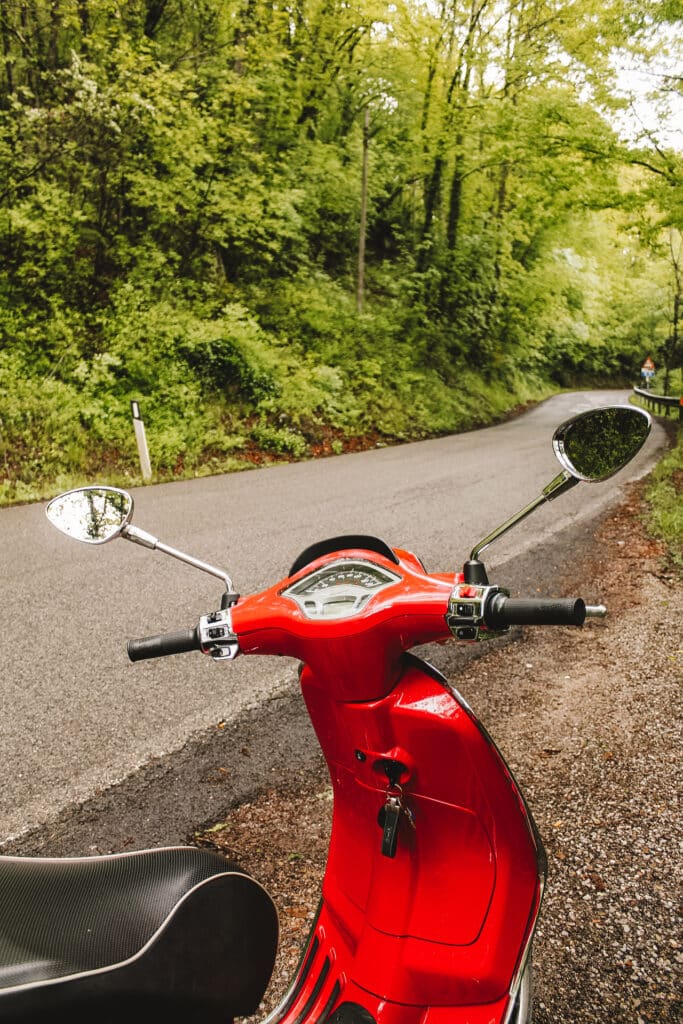 Rode Vespa staat langs de kant van de weg.