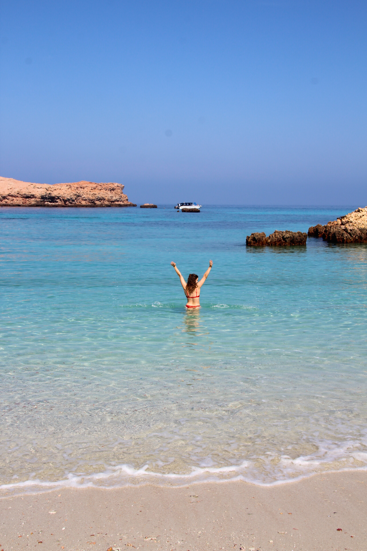Lotte draagt een rode bikini, steekt haar armen in de lucht terwijl ze zwemt in het heldere water van Daymaniat Island.