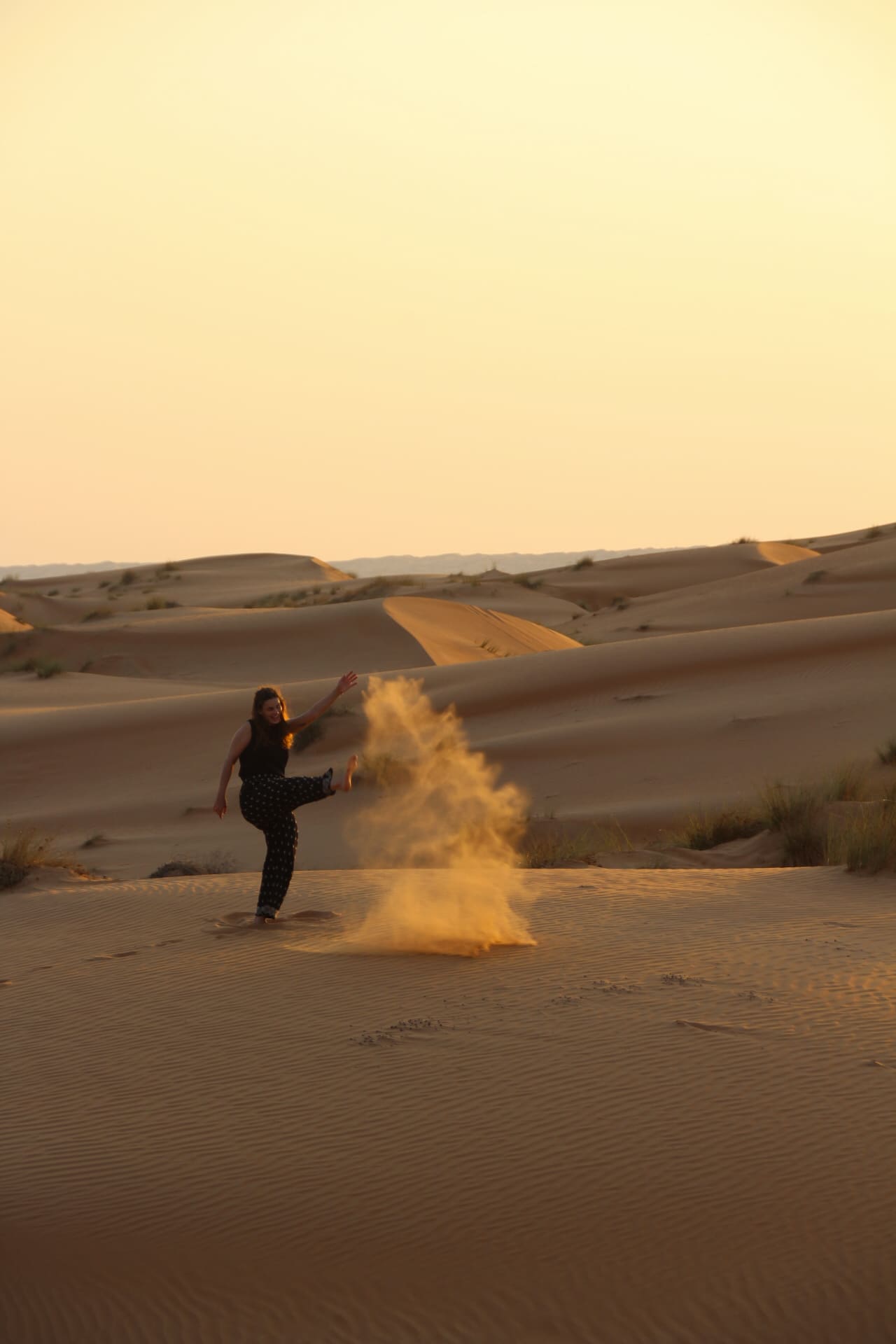 Lotte speelt in het zand van de duinen in Wahiba Sands, Oman tijdens de zonsondergang.