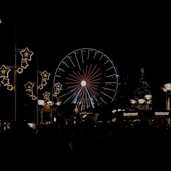 Kerstmarkt van Duisburg in Duitsland, met in de verte een verlicht reuzenrad en aan de zijkanten straatverlichting in de vorm van sterretjes.